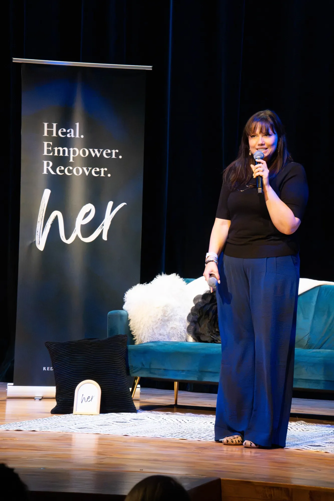 Brooke on stage at the HER. launch in front of the Heal, Empower, Recover banner
